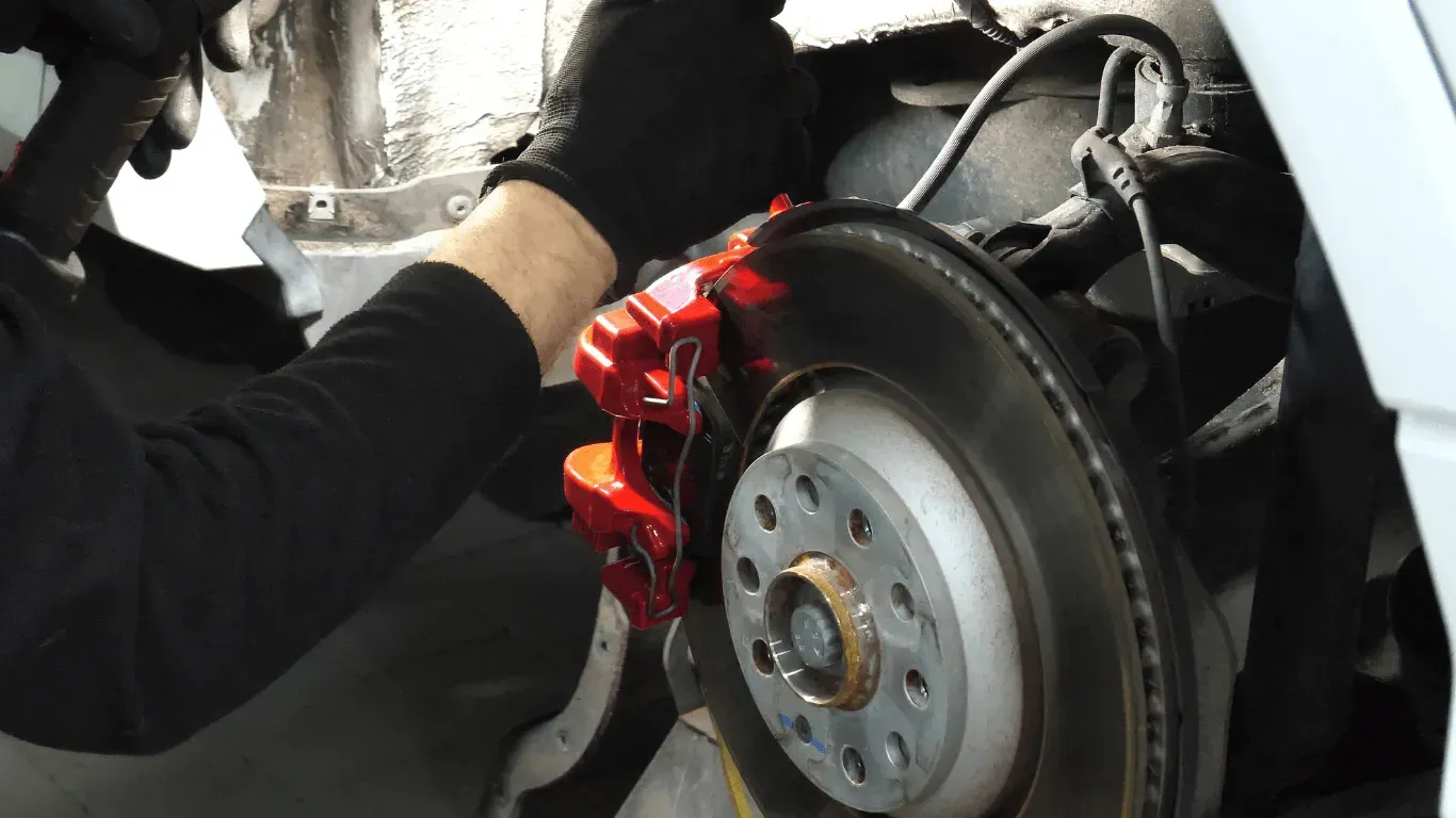 Close-up of a mechanic installing new red brake calipers on a car.