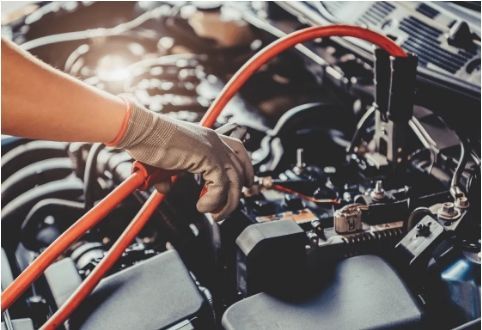 Technician using jumper cables to test or jump-start a car battery.