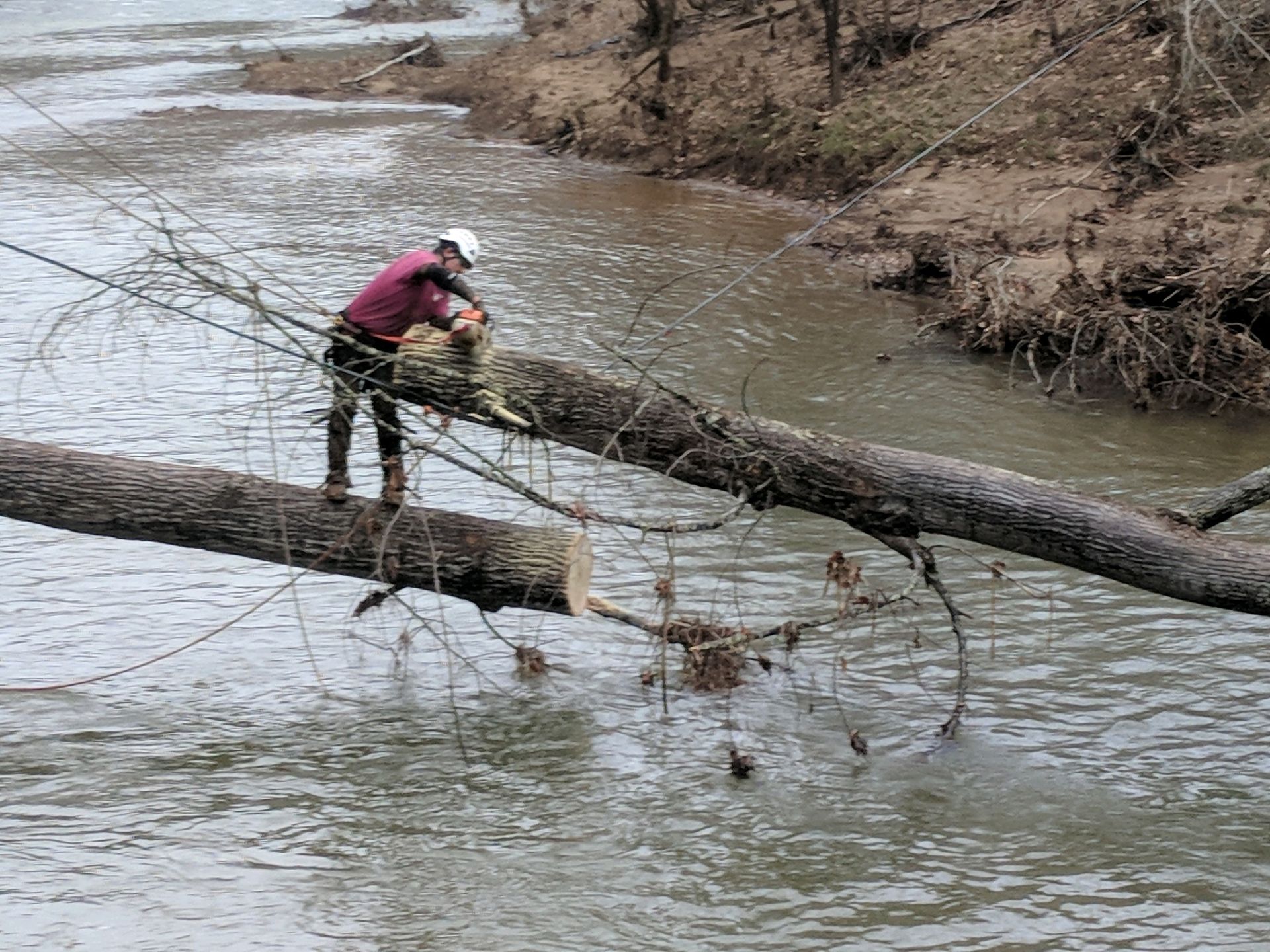A man is sitting on a log in the middle of a river.