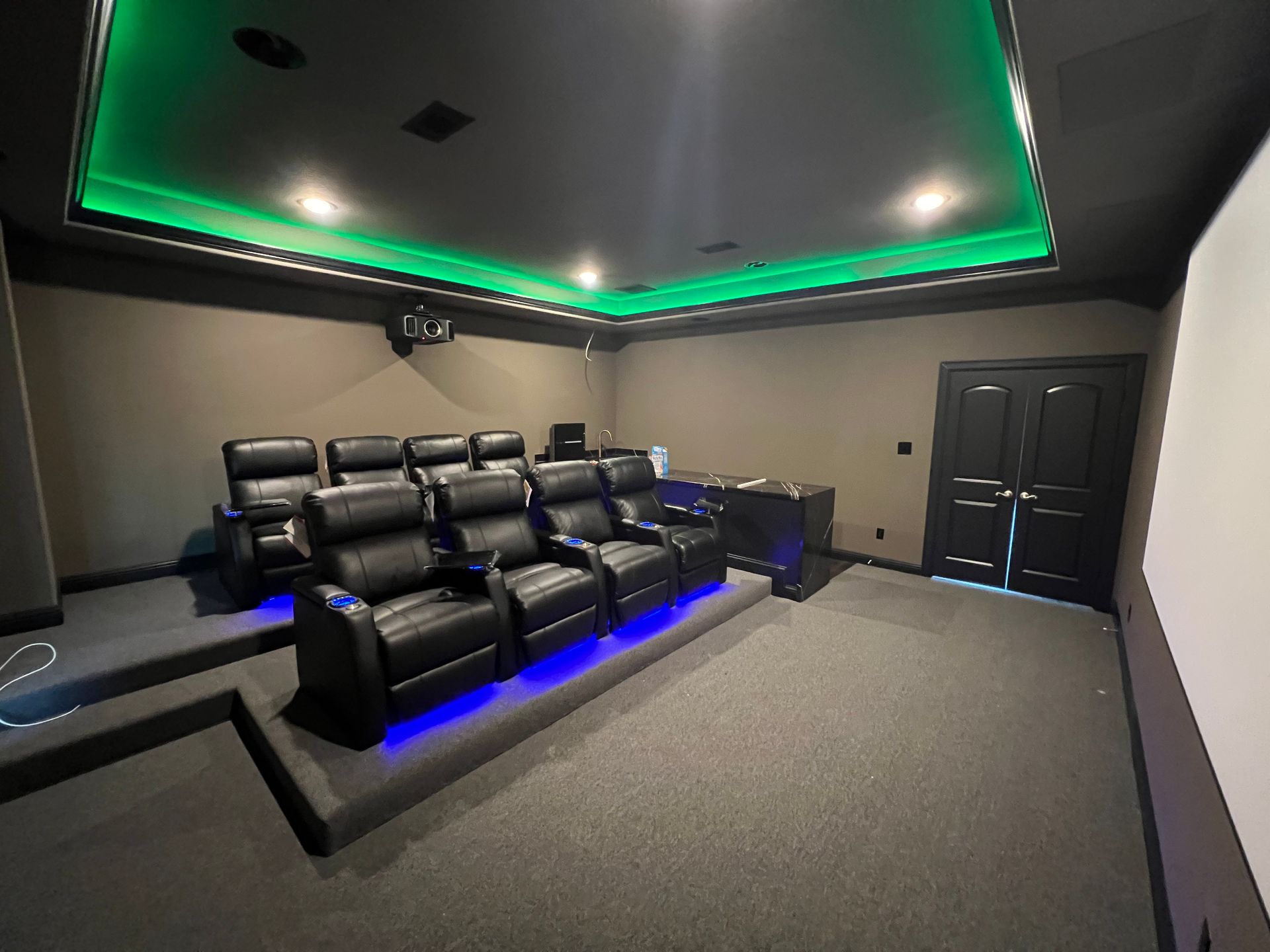 A home theater with black leather seats and green lights on the ceiling.