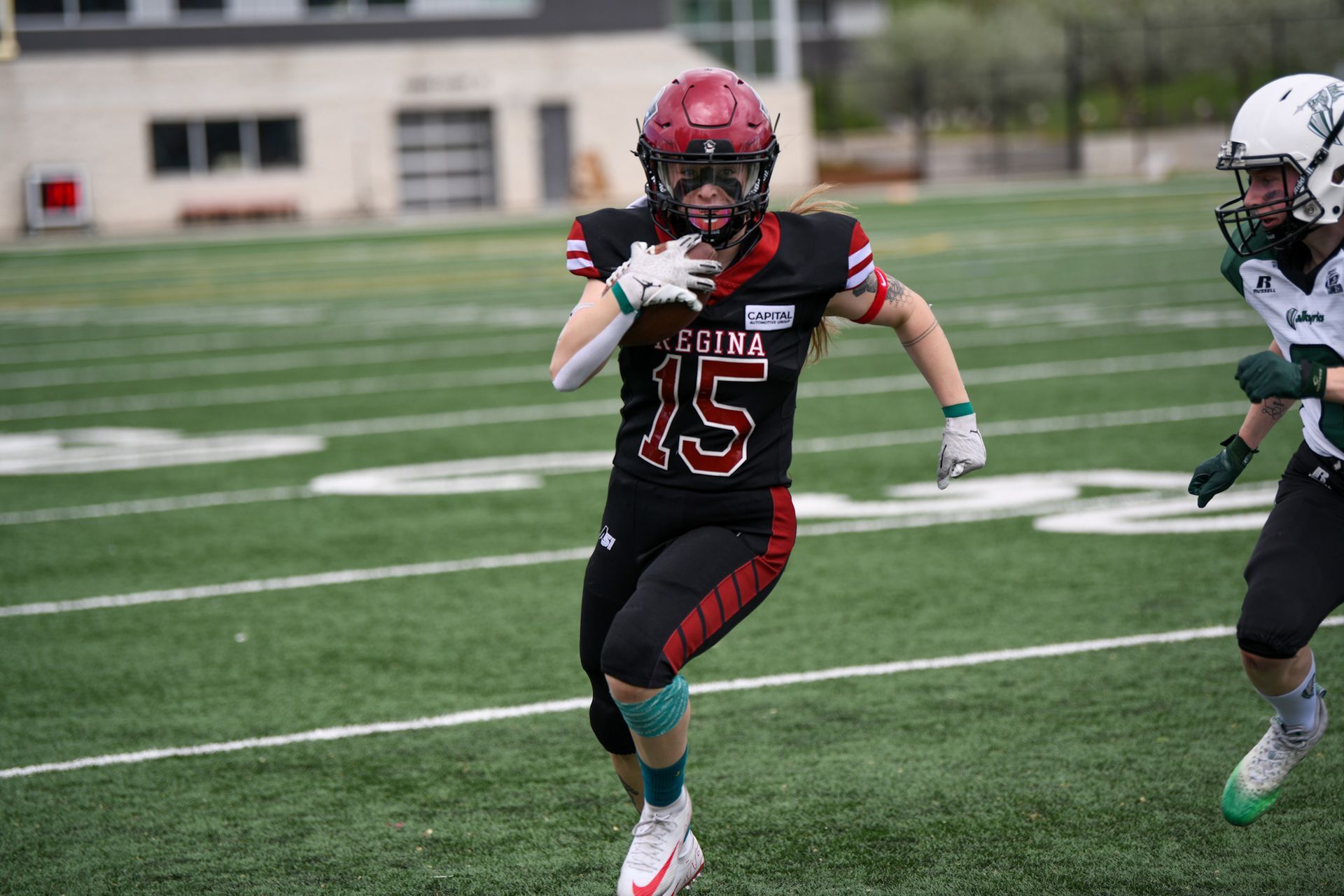 Football player in black uniform with number 15 runs on a green field, carrying the ball.