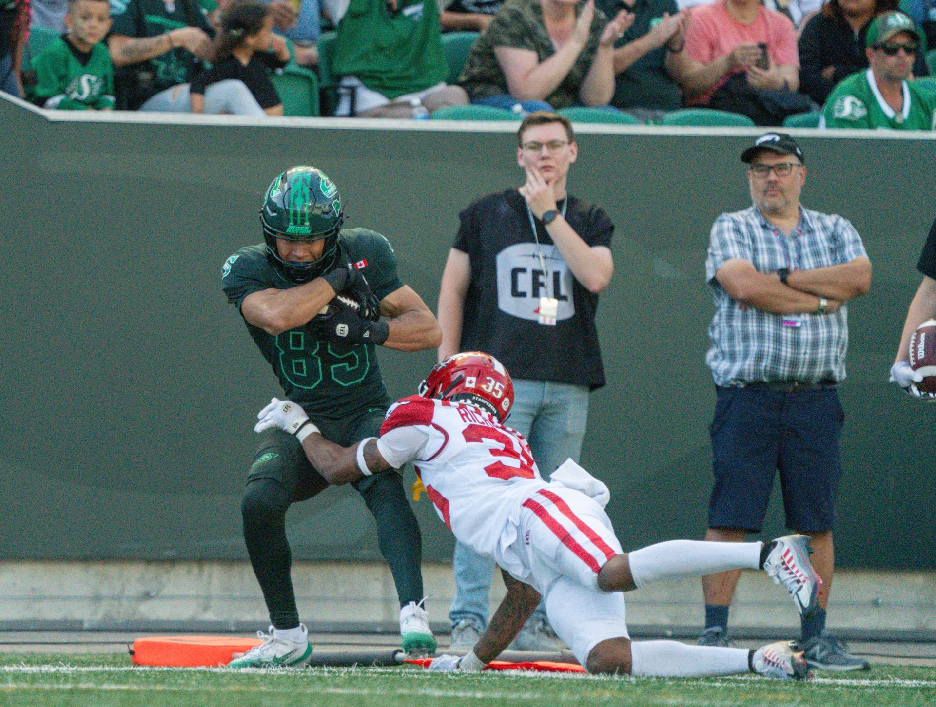 Football player in green uniform tackled near end zone by player in red uniform.