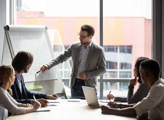 A man is giving a presentation to a group of people sitting around a table.