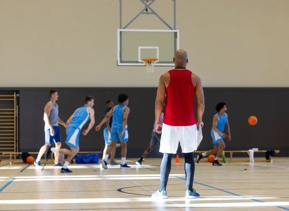 A man in a red tank top is watching a basketball game.