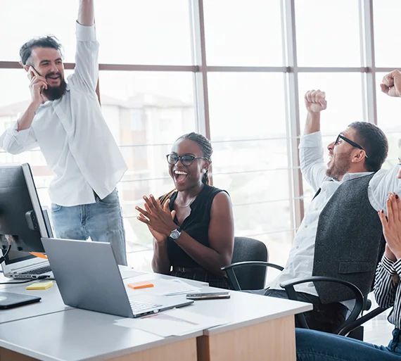 A group of people are sitting at a desk with their arms in the air.