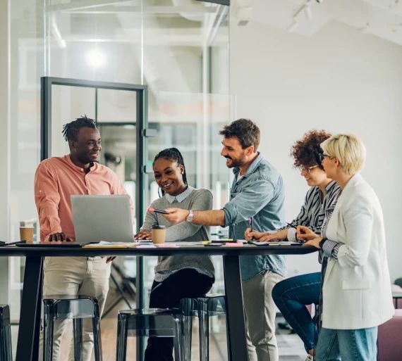 A group of people are standing around a table with a laptop.