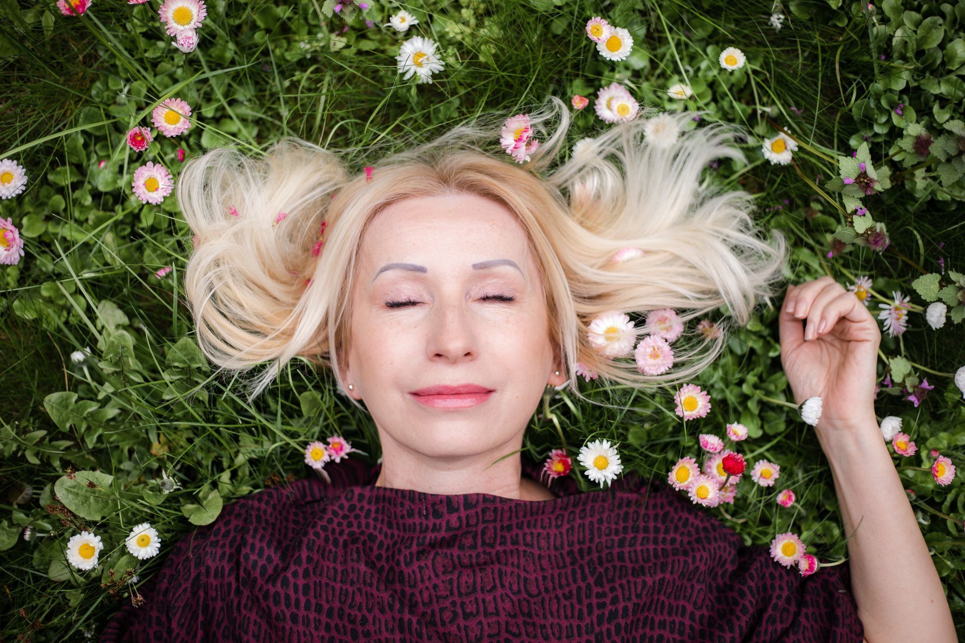 Serene elderly woman experiencing peace during menopause, lying on grass with eyes closed.