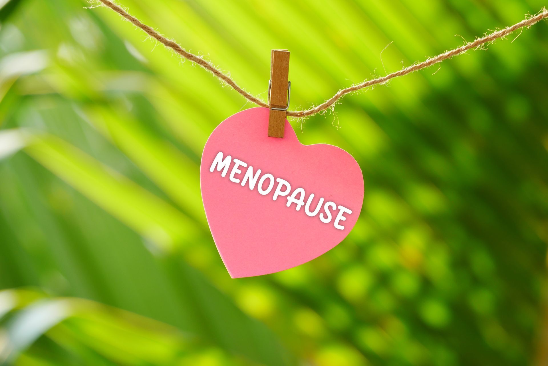 Pink heart note paper with the word Menopause hanging on a string, symbolizing women’s health. Pink heart note paper with the word Menopause hanging on a string, symbolizing women’s health.