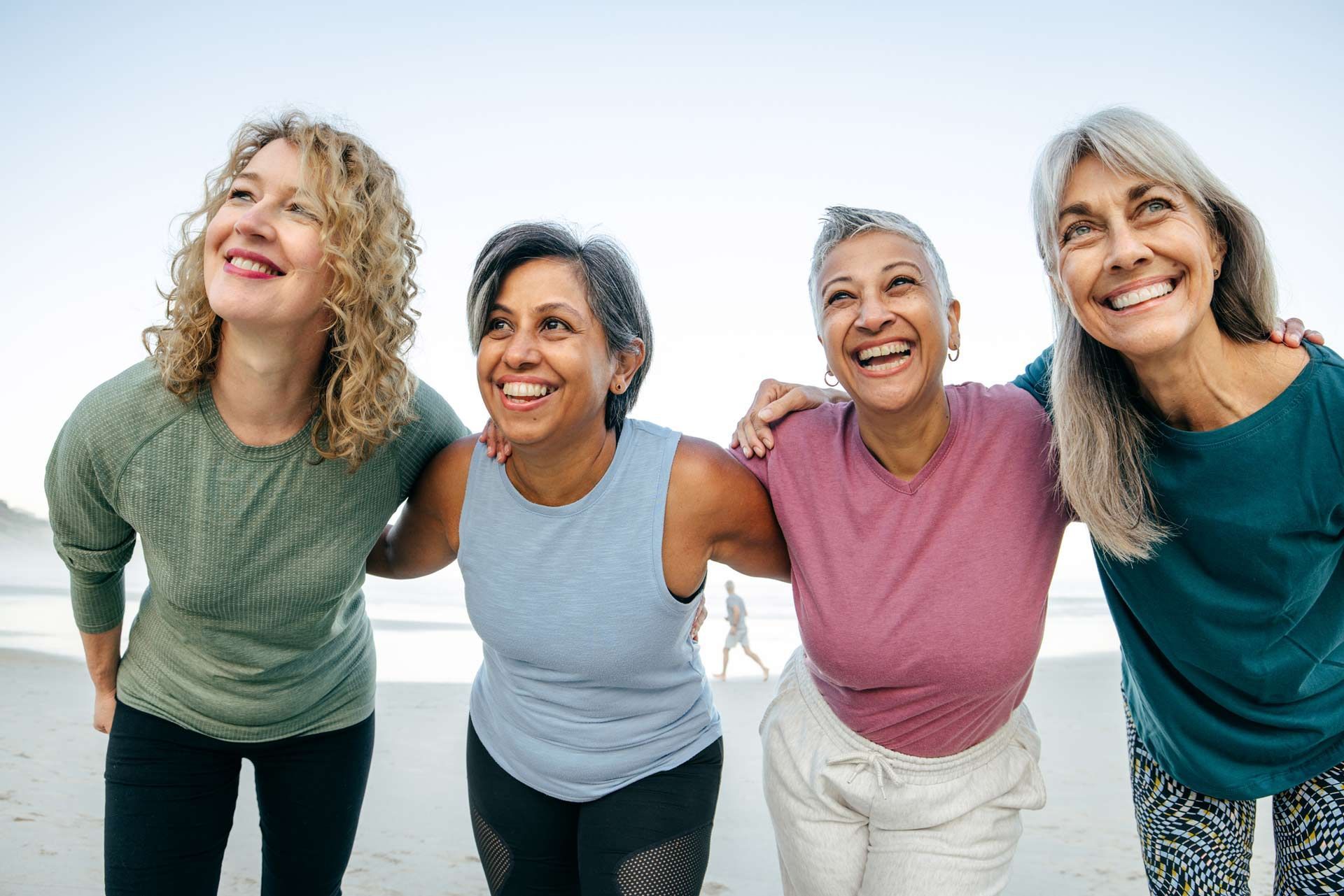 A group of middle-aged sporty women stands together on the beach, dressed in athletic wear. A group of middle-aged sporty women stands together on the beach, dressed in athletic wear.