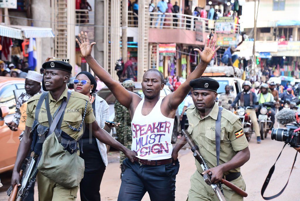 A man holding a sign that says speaker must sign is being arrested by police