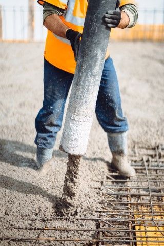 Construction worker pours concrete from a hose onto rebar, wearing an orange vest and gloves.
