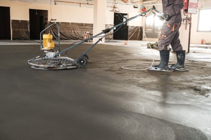 Person using a floor grinder in an unfinished room, smoothing a concrete surface.