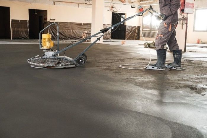 Person using a floor grinder in an unfinished room, smoothing a concrete surface.