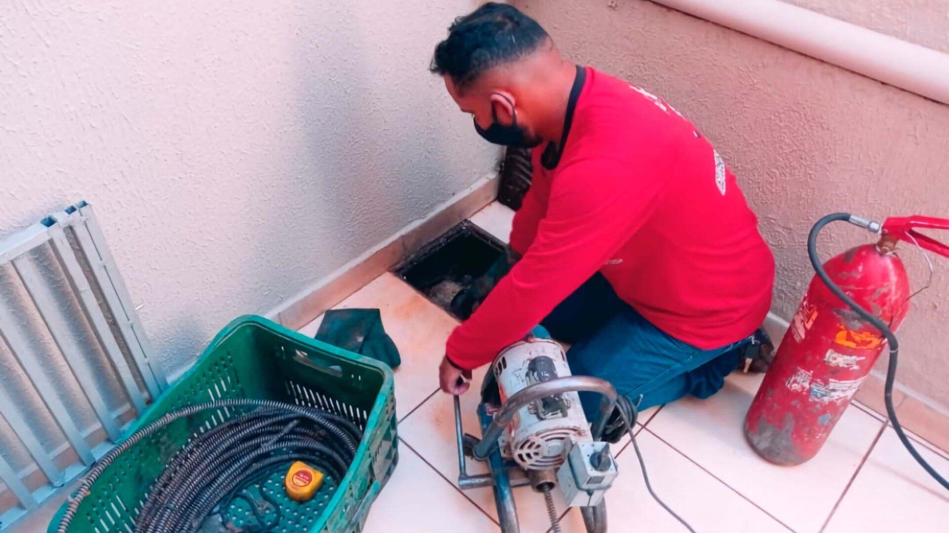 Um homem de camisa vermelha está ajoelhado no chão usando uma máquina.