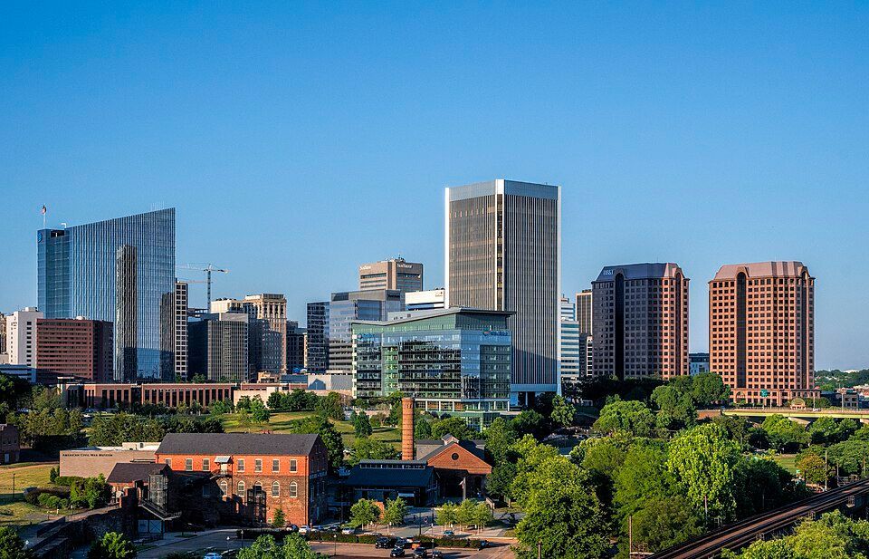 Skyline of Richmond, Virginia with tall buildings, blue sky, and green trees in the foreground.