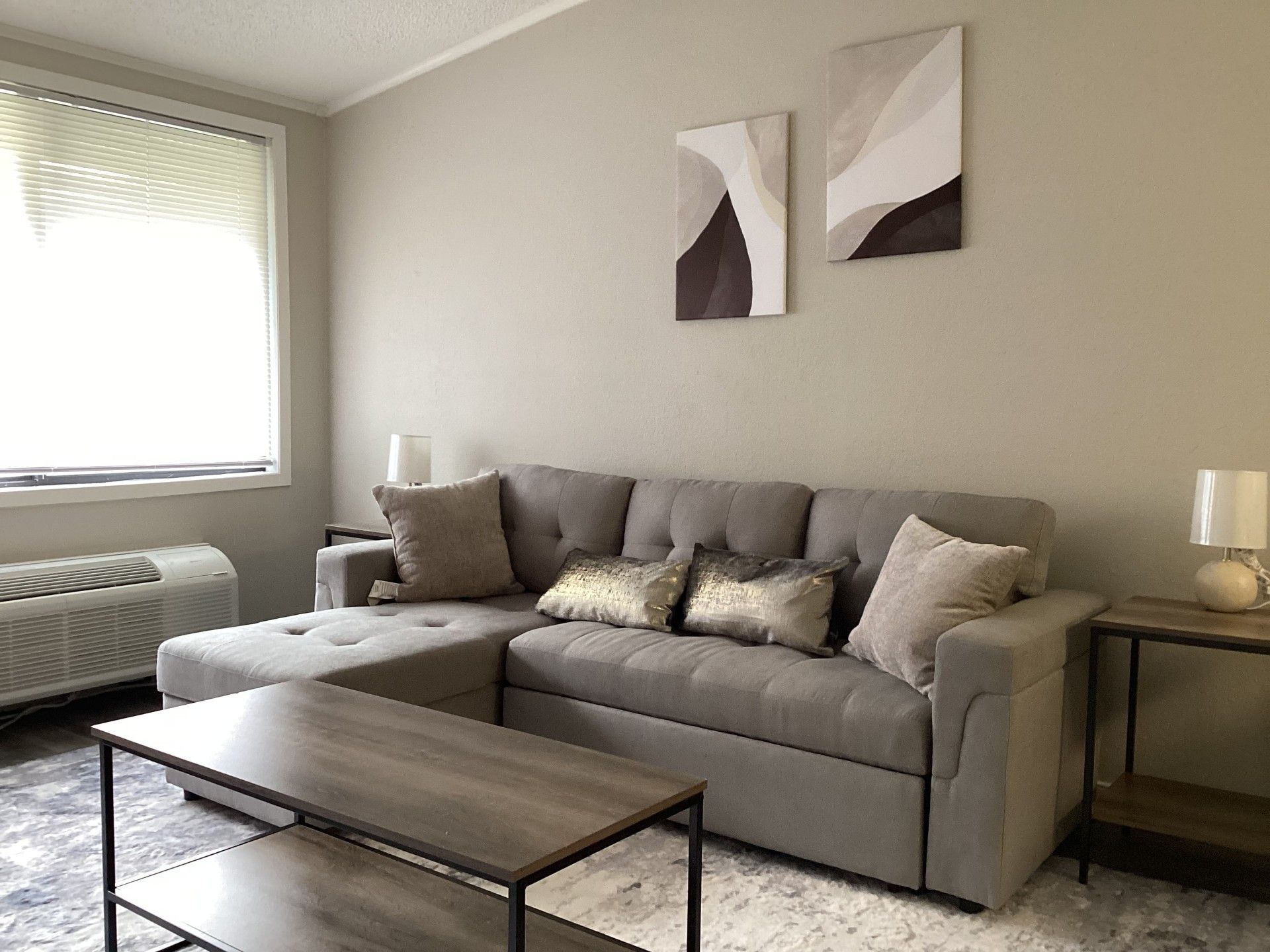 Living room with gray sectional sofa, coffee table, window, and abstract art.