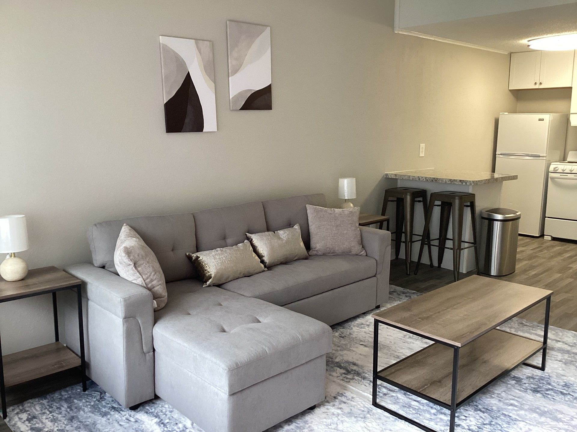 Living room with gray sectional sofa, art, coffee table, and kitchen with bar stools.