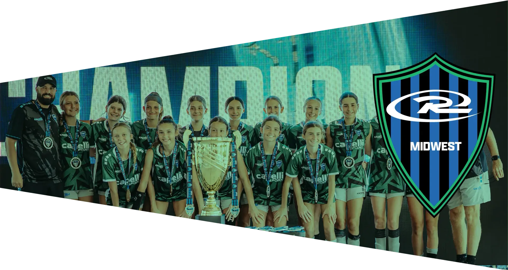 A soccer team wearing black and teal jerseys stands behind a trophy in front of a