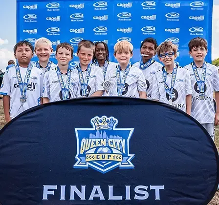 Youth soccer team with medals posing in front of a banner at the Queen City Cup.
