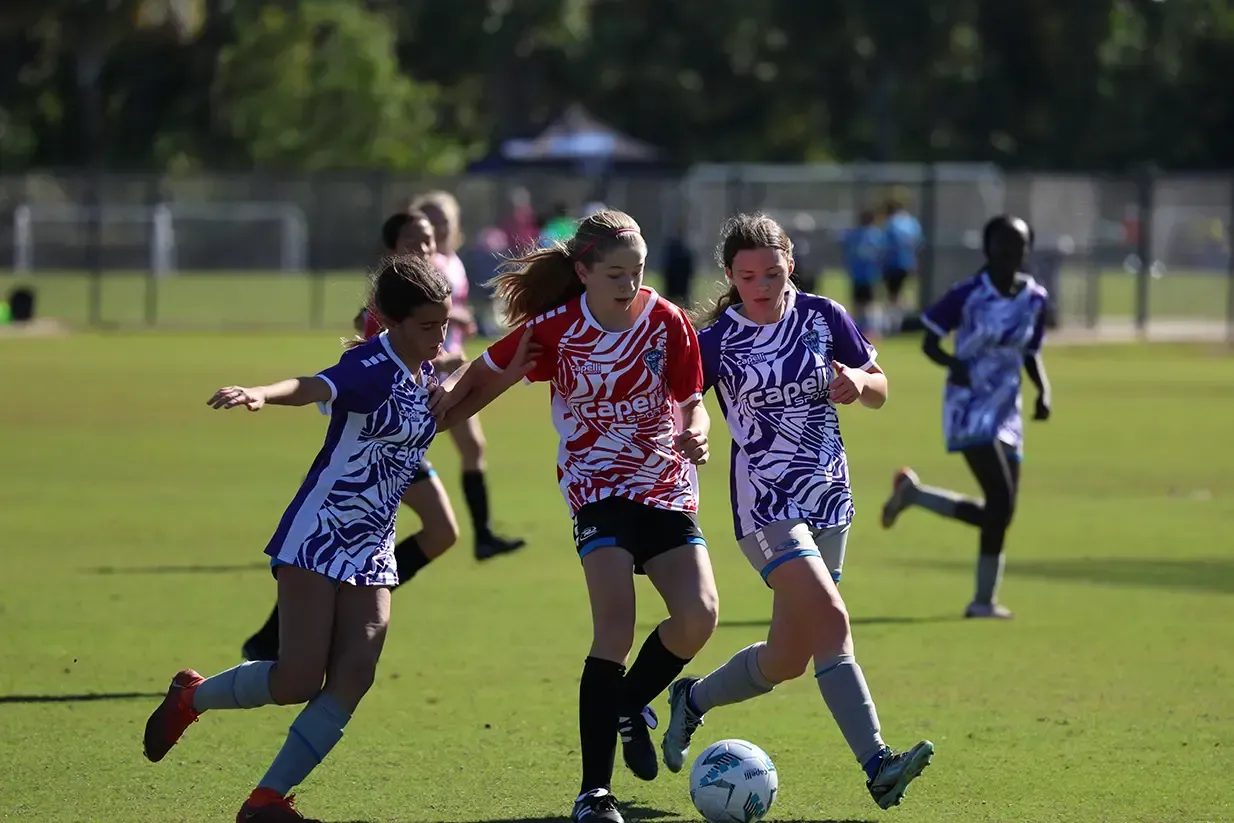 Soccer players on a field, one in red, two in purple, chasing the ball.