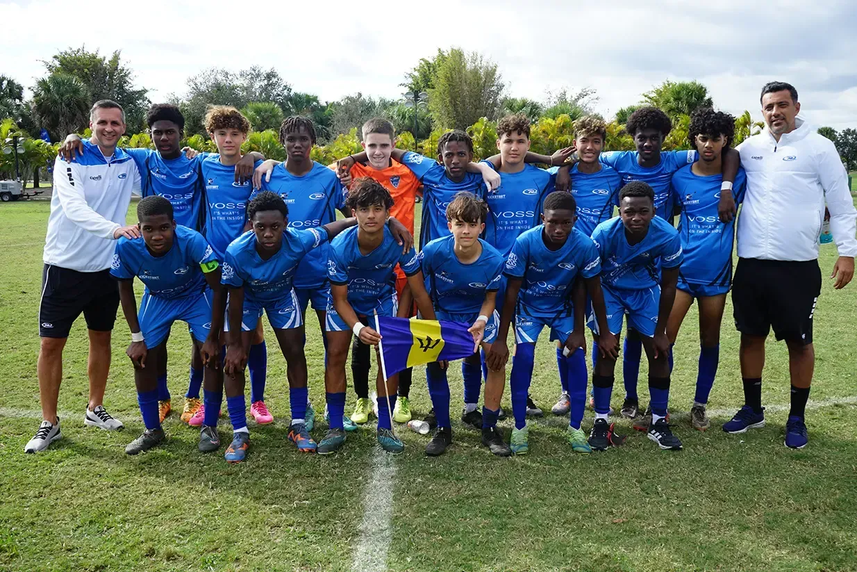 Soccer team in blue uniforms poses on grass field with coaches.