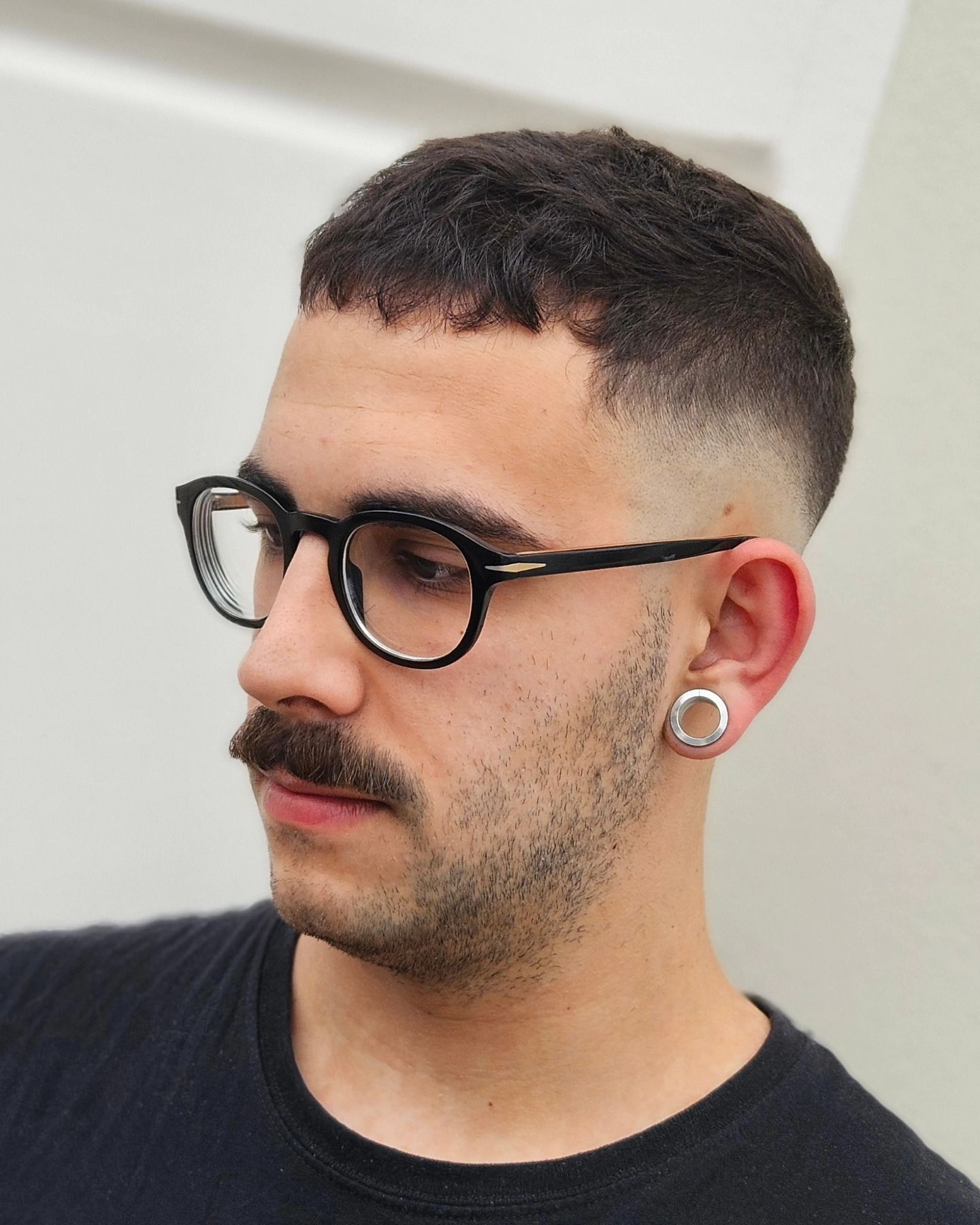 Un uomo con gli occhiali e i baffi indossa una camicia nera