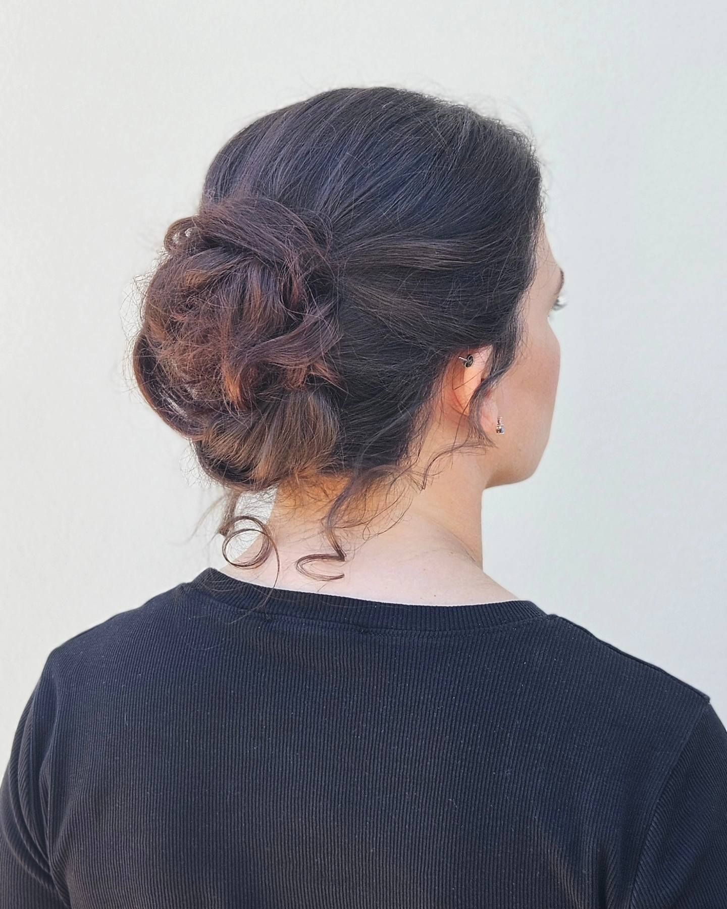 La schiena di una donna che indossa una camicia nera e ha i capelli raccolti in uno chignon.