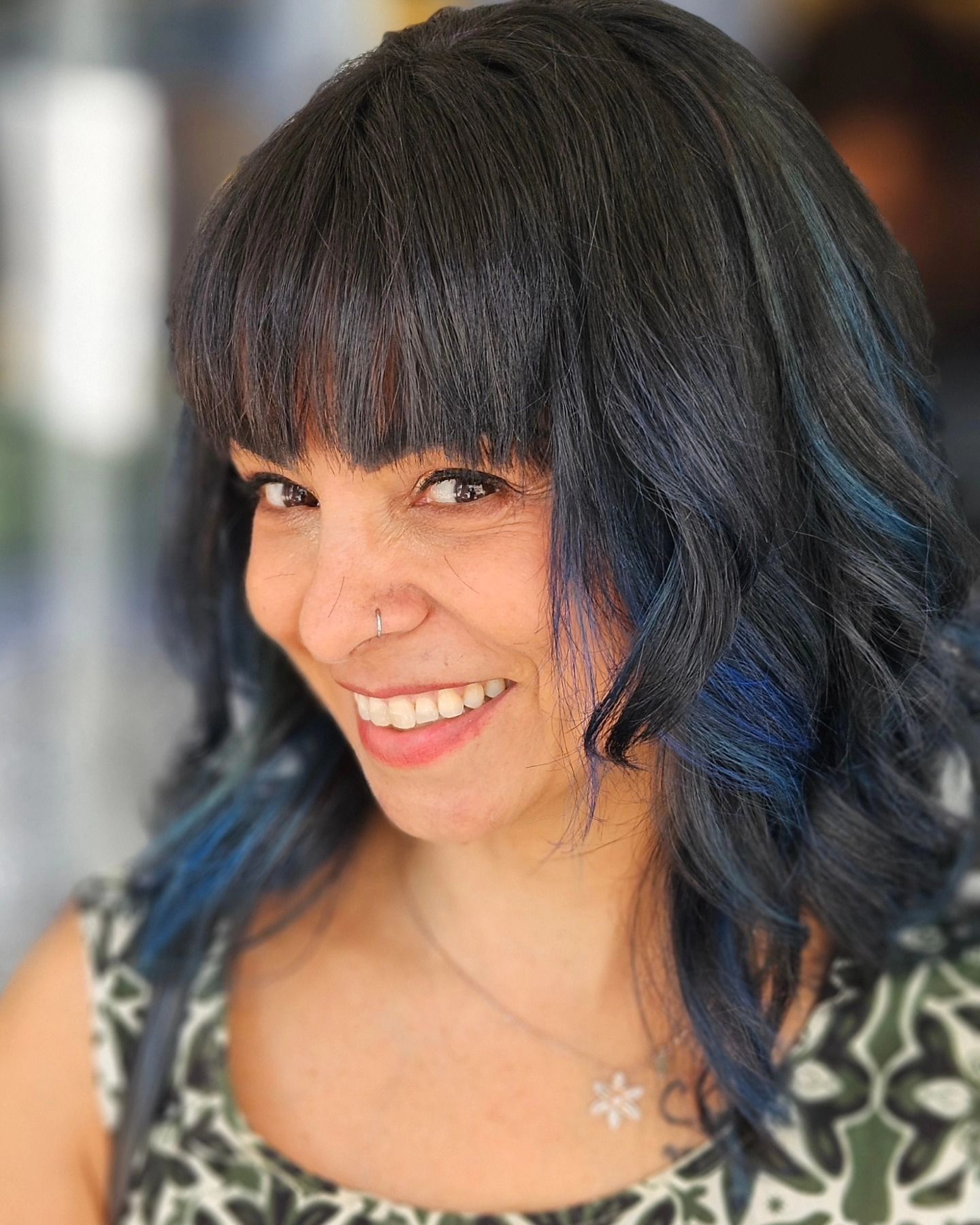 Una donna con i capelli blu e un anello al naso sorride.