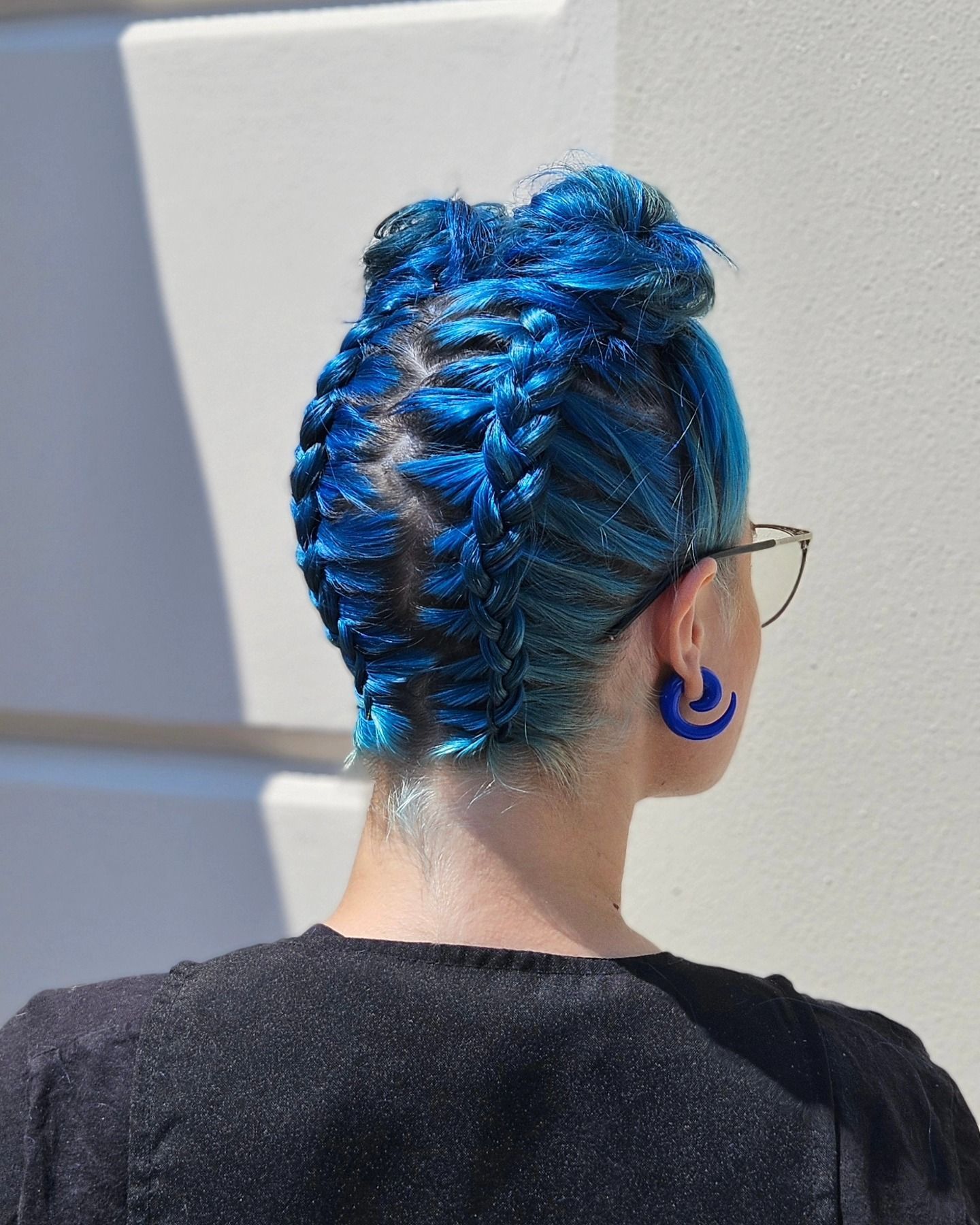Una donna con i capelli blu indossa occhiali e orecchini blu