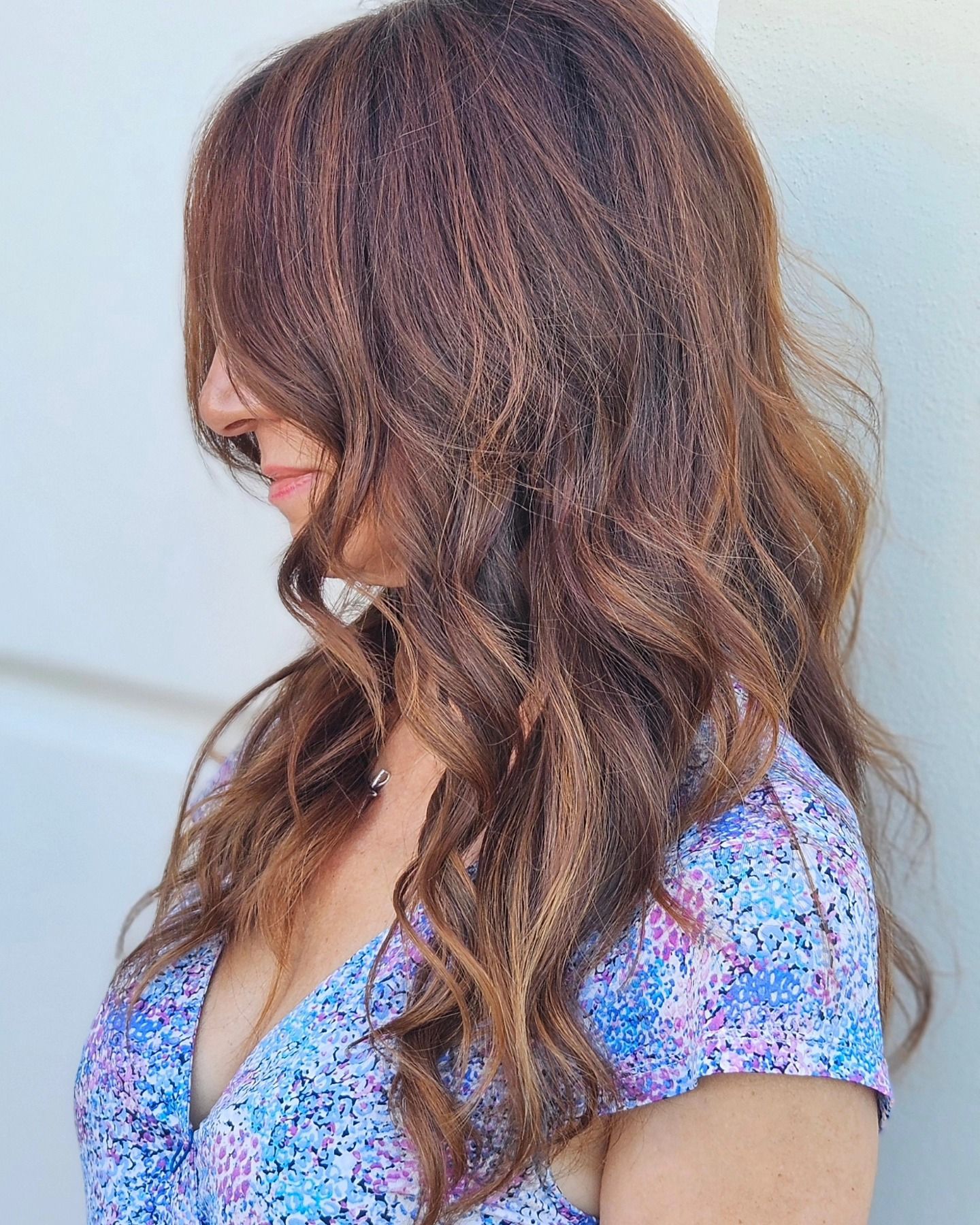 Una donna con lunghi capelli castani indossa un vestito blu e viola.