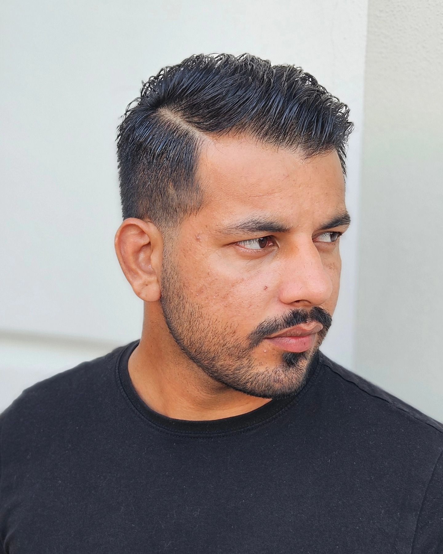 Un uomo con barba e baffi indossa una camicia nera.