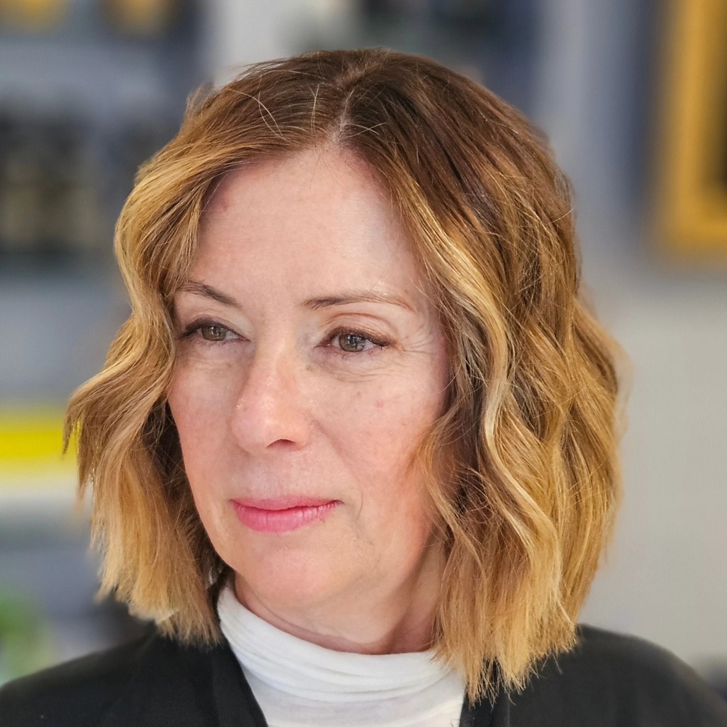 Una donna con i capelli biondi corti indossa una giacca nera e un dolcevita bianco.