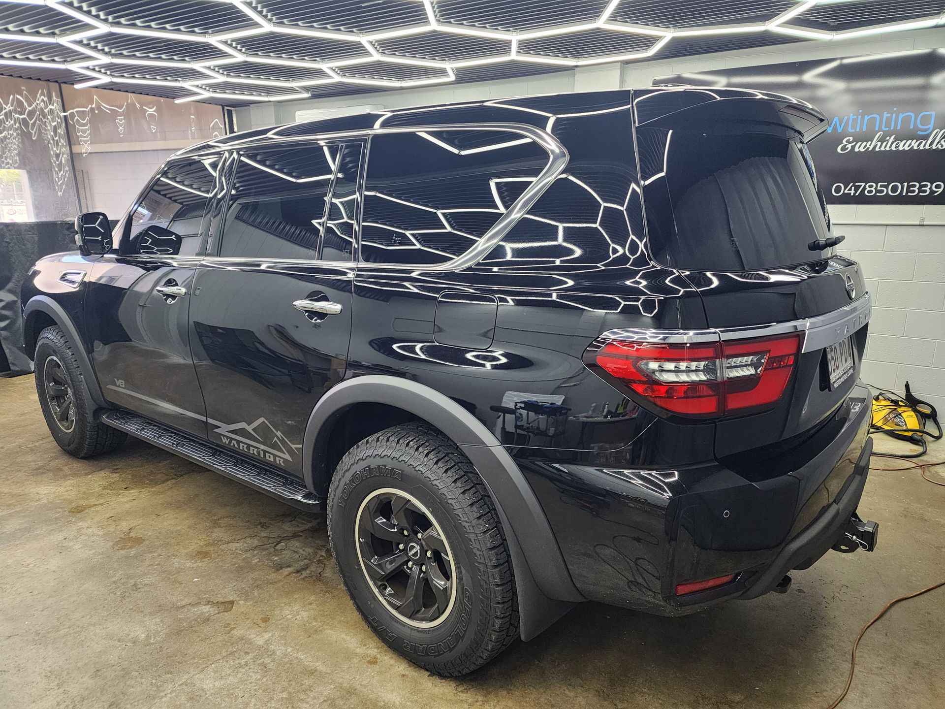 White SUV in a showroom, rear view with tinted windows and hexagonal ceiling lights reflected on the glass — Superior Window Tinting & Whitewalls in Portsmith, QLD
