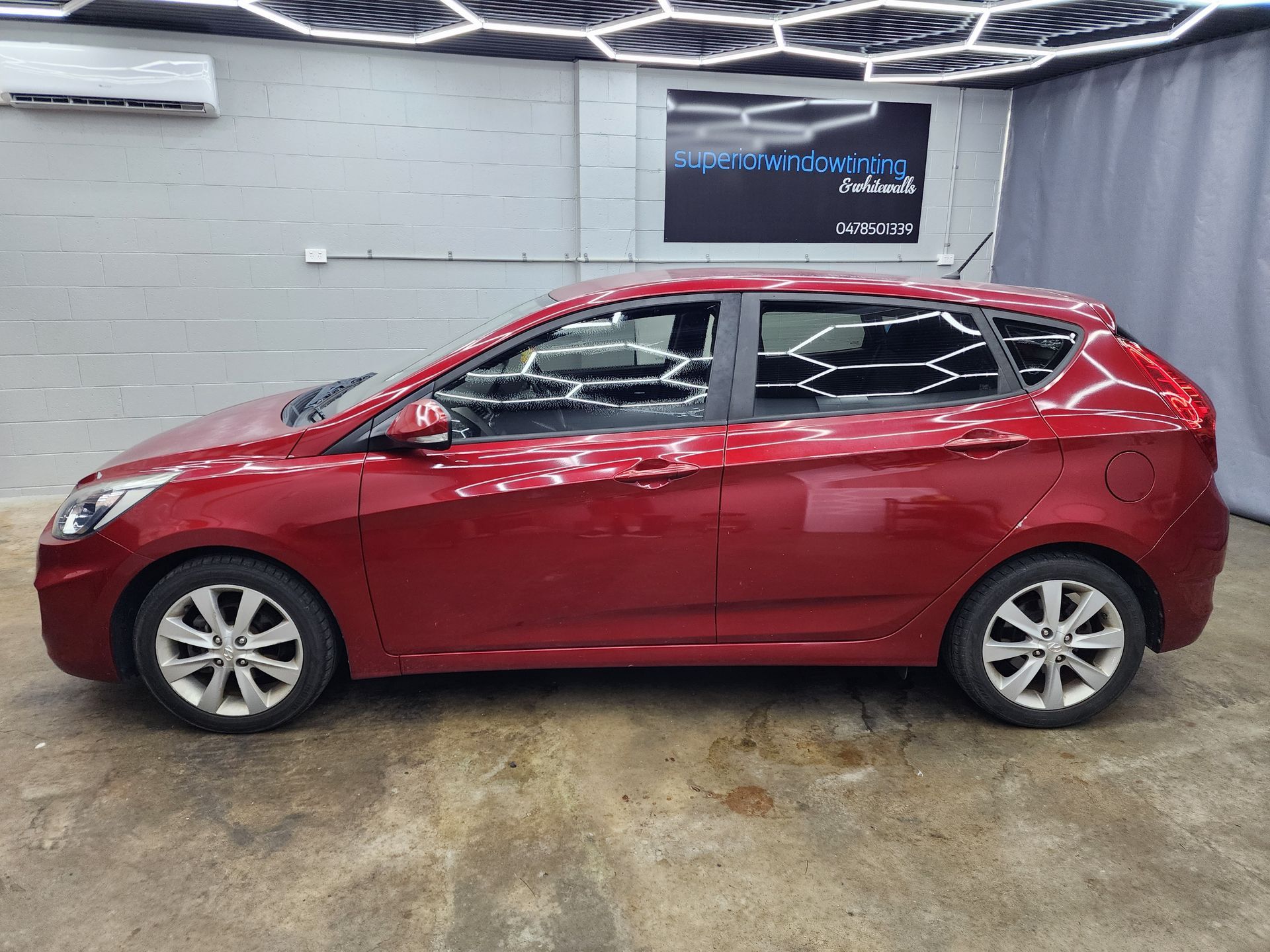 Red hatchback car parked indoors in a showroom, side view on a concrete floor — Superior Window Tinting & Whitewalls in Portsmith, QLD