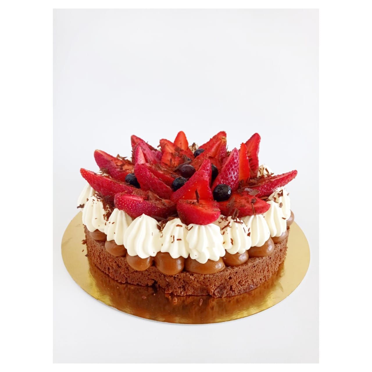 Pastel de chocolate cubierto con fresas, crema batida y virutas de chocolate sobre una base de pastel dorada.