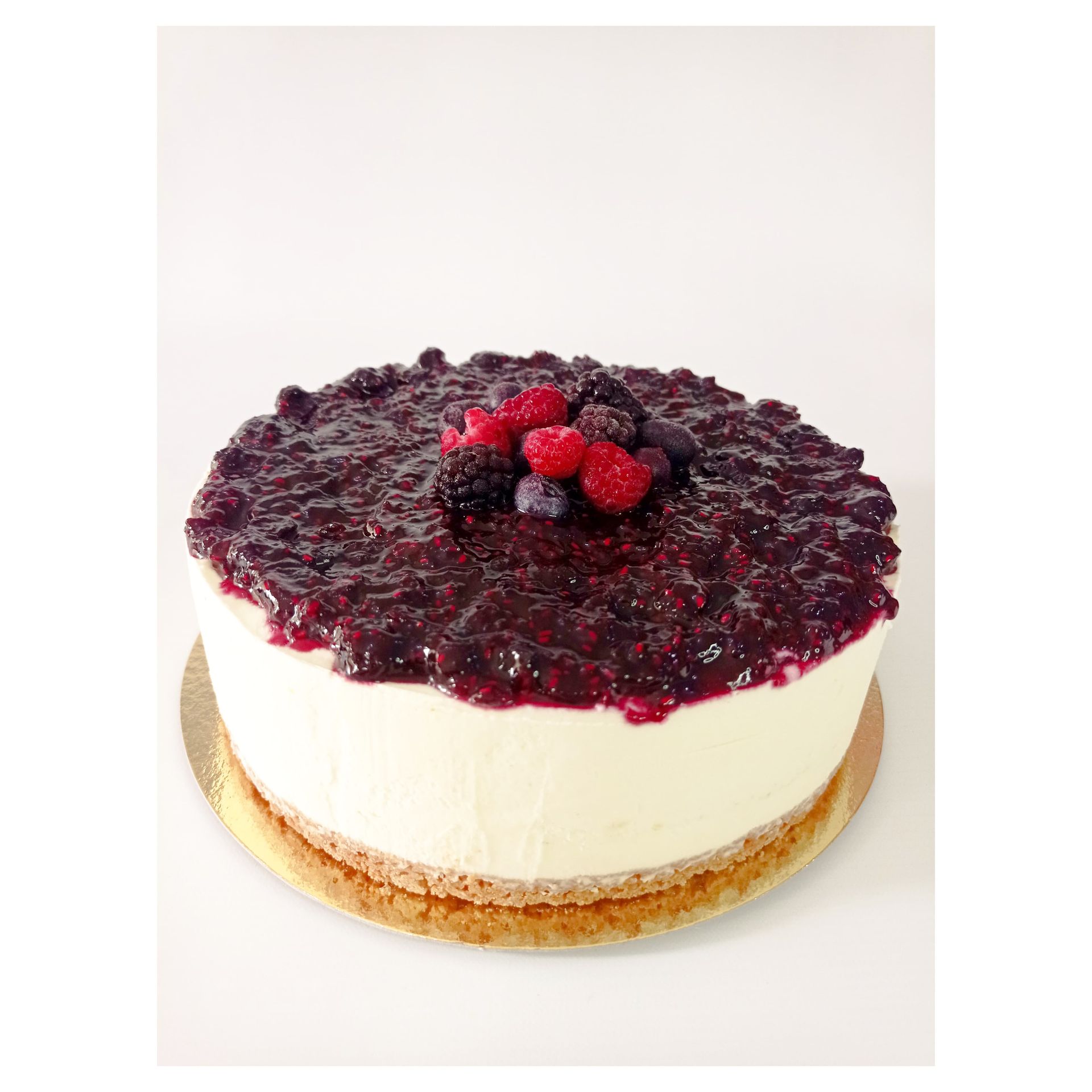 Tarta de queso cubierta con compota de frutos rojos y bayas frescas sobre una base dorada, sobre un fondo blanco.