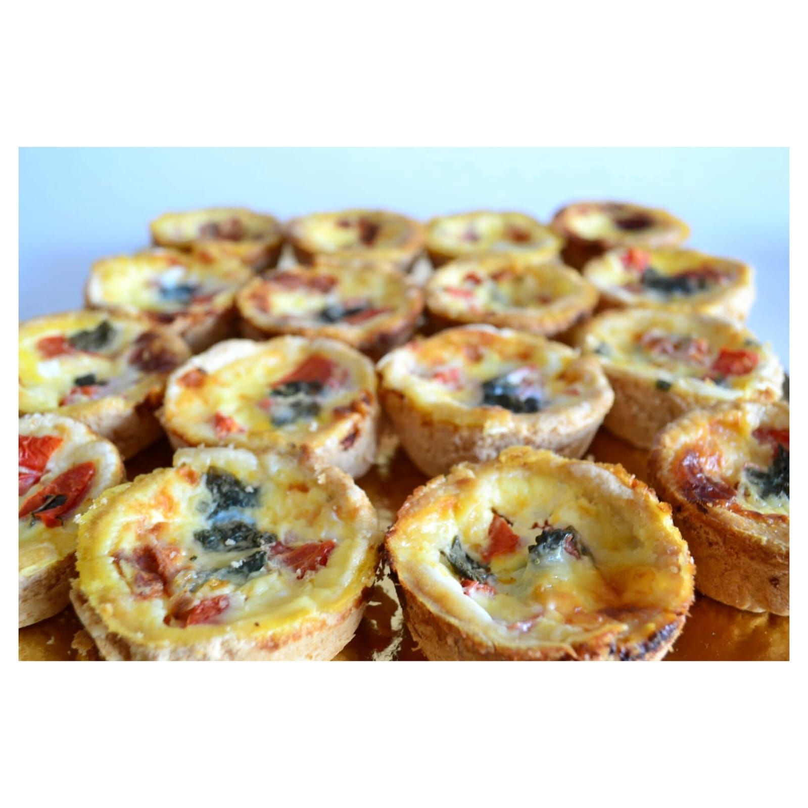 Mini quiches con corteza dorada, rellenas de queso, tomate rojo y espinacas verdes.