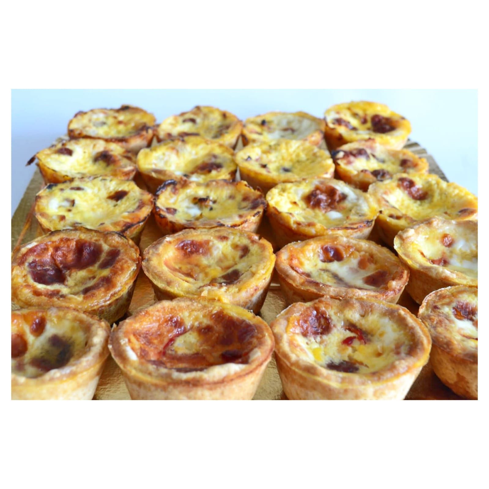 Mini quiches en bandeja dorada, horneadas con corteza dorada y relleno de crema pastelera.