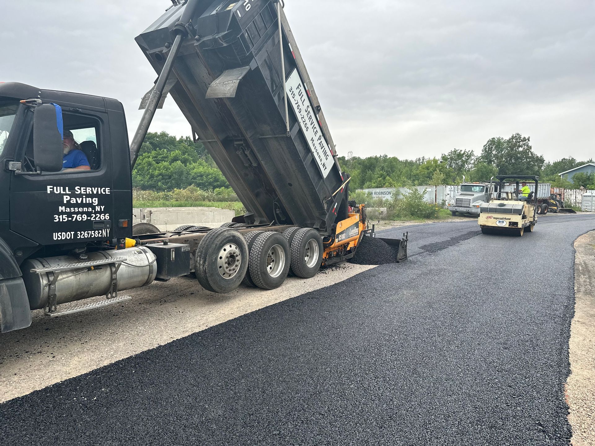 A dump truck is being loaded with asphalt on a road.