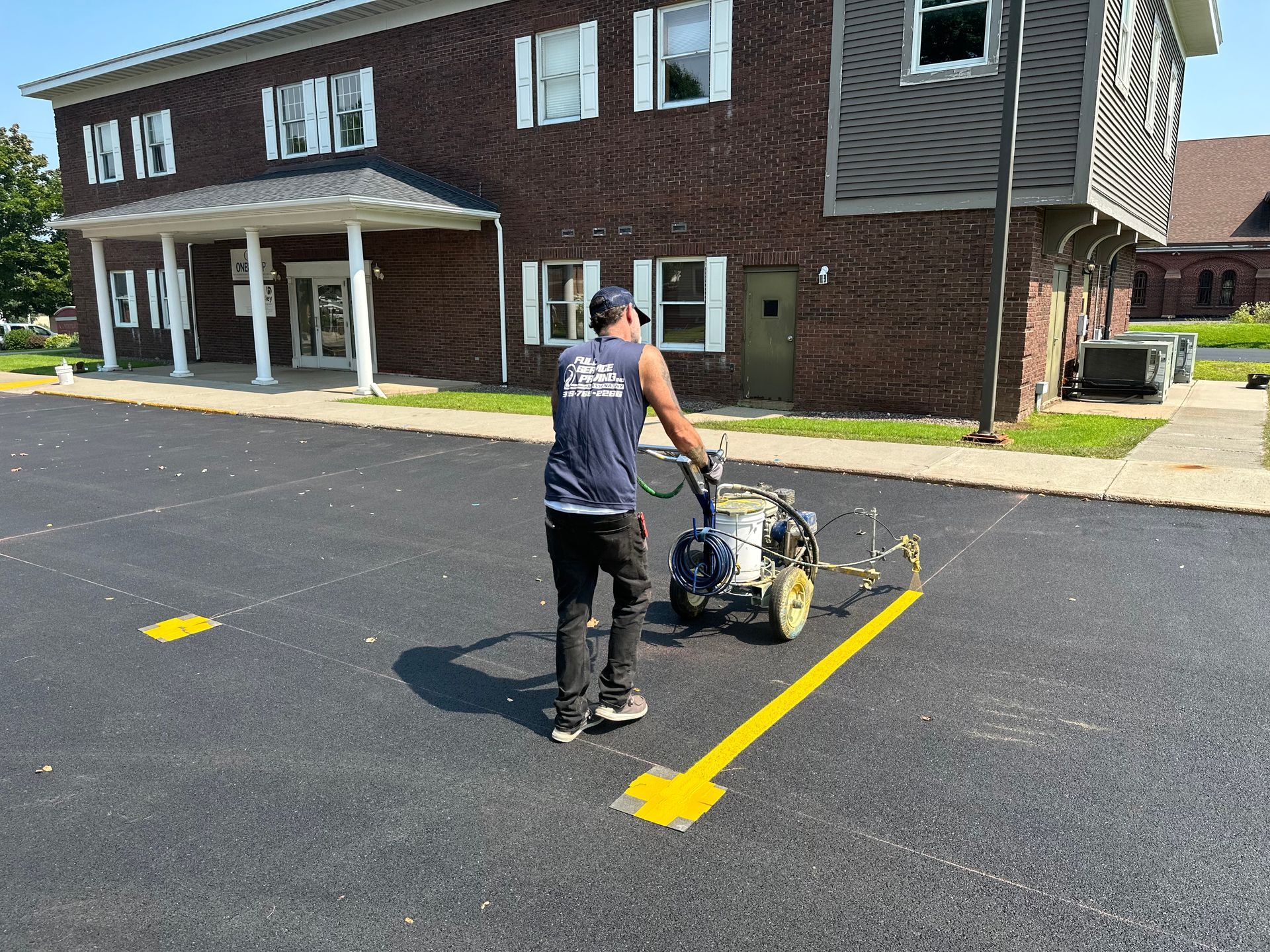 A man is using a machine to paint a yellow line on a parking lot.