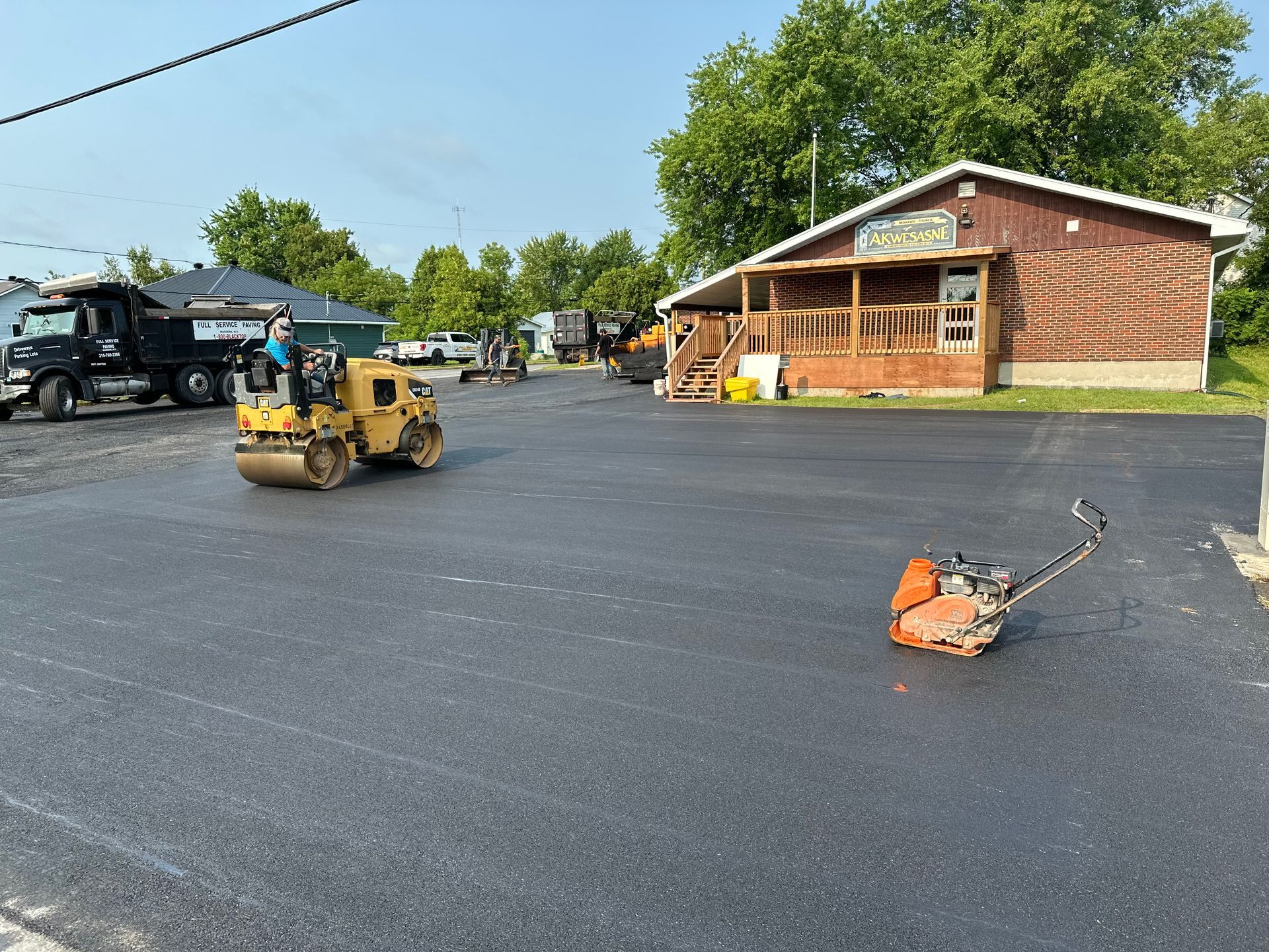 A roller is rolling asphalt in a parking lot in front of a building.