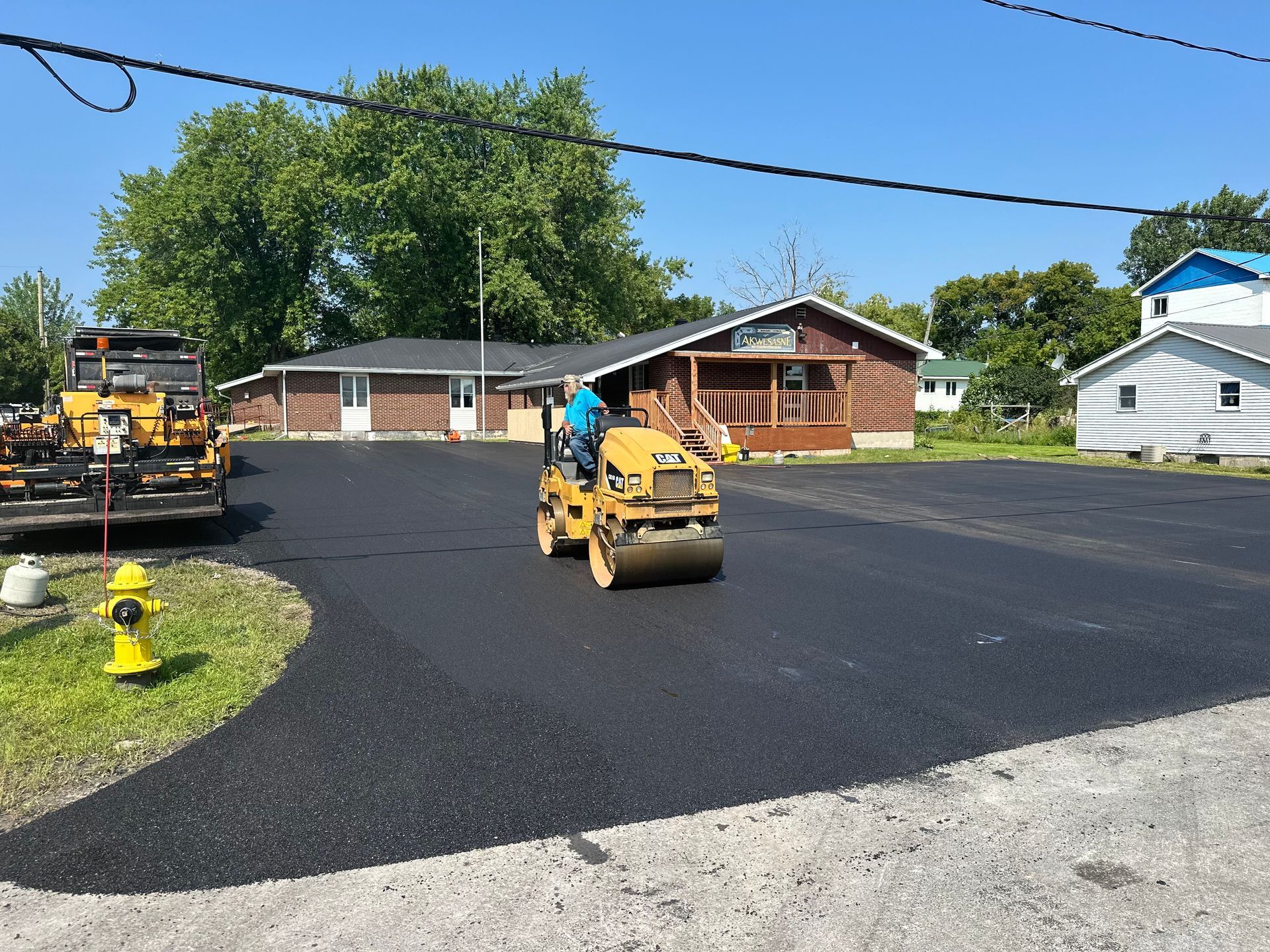 A man is driving a roller on a road in front of a house.