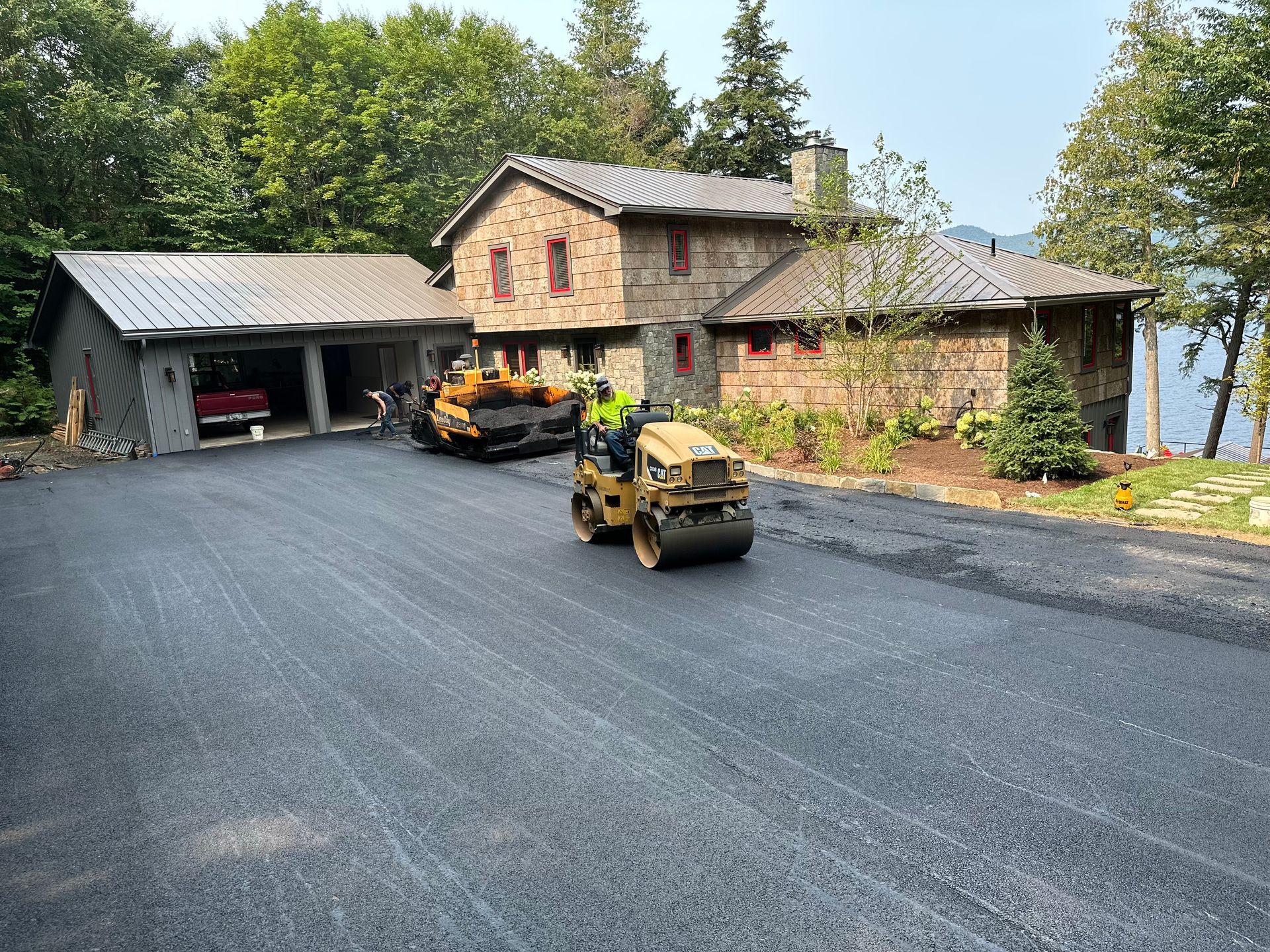 A man is driving a roller on a road in front of a large house.