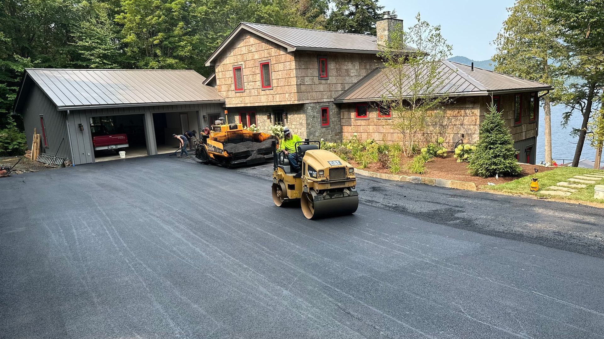 A man is driving a roller on a road in front of a large house.