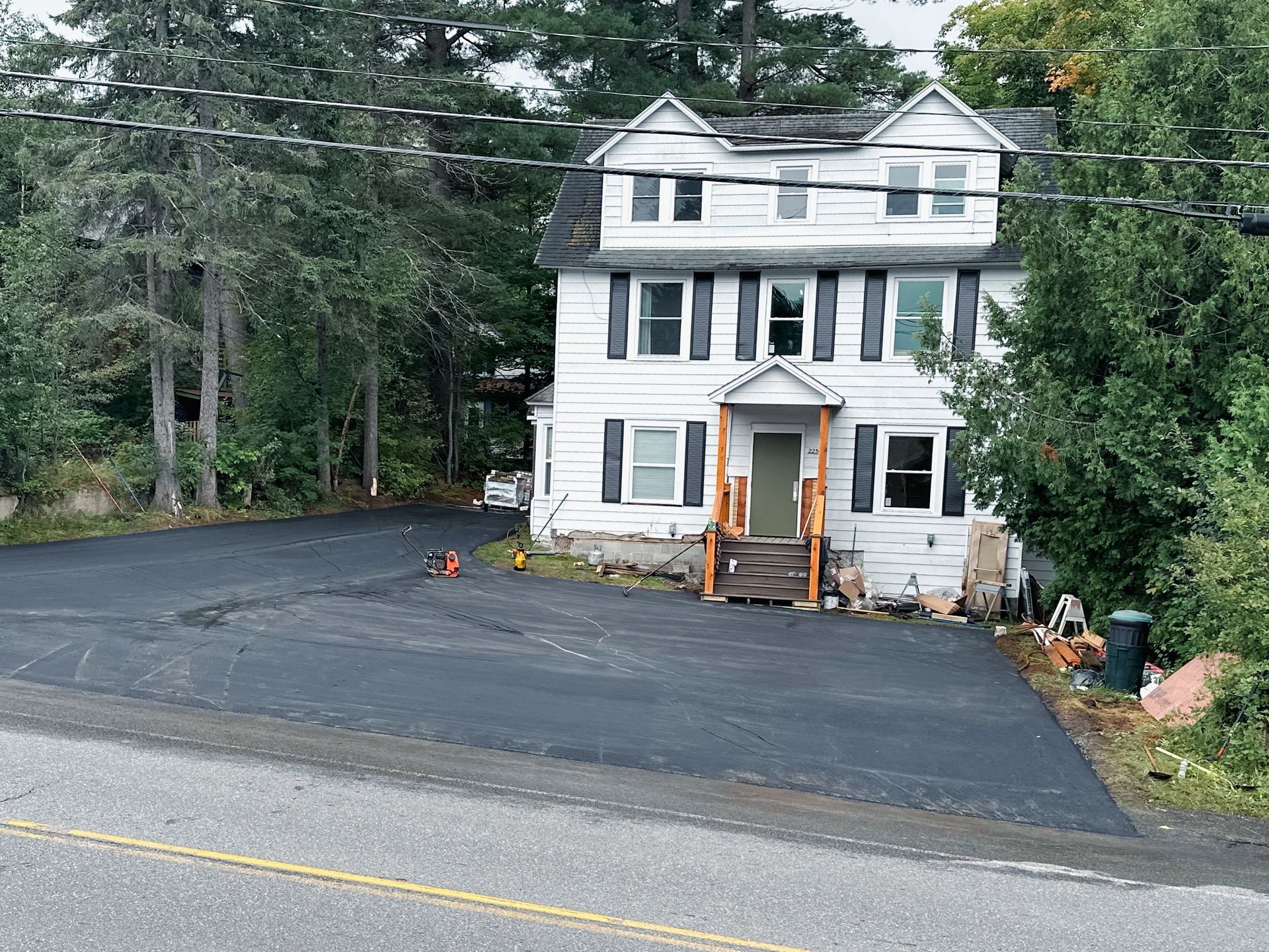 A large white house is sitting on the side of a road surrounded by trees.