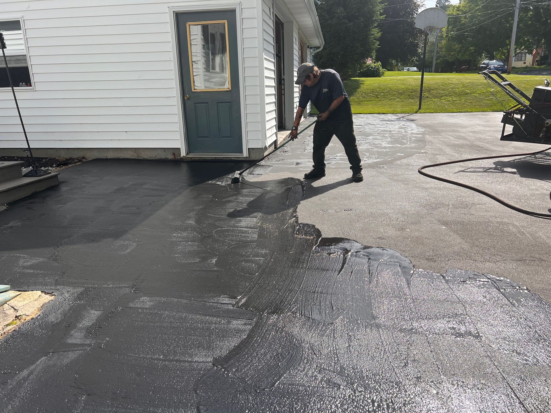 A man is applying asphalt to a driveway in front of a house.