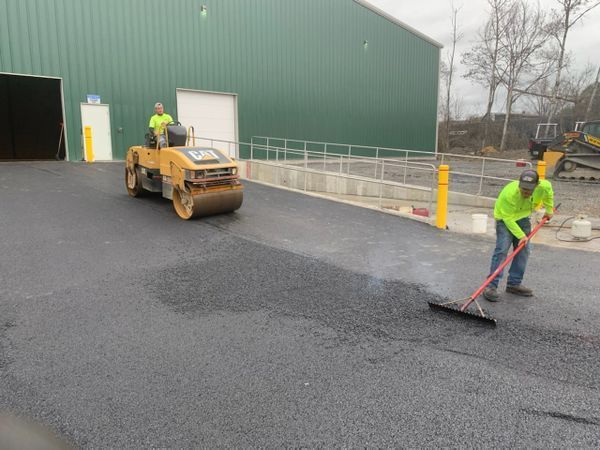 Two men are working on a road with a roller and a broom.