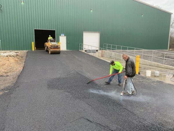 Two men are working on a road in front of a building.