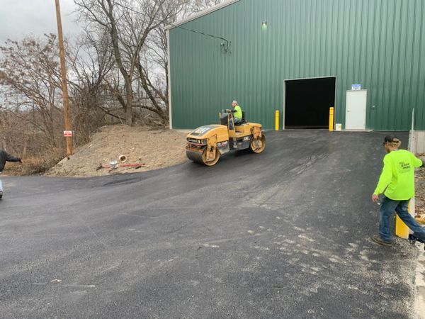 A man in a green shirt is standing next to a roller on a road.