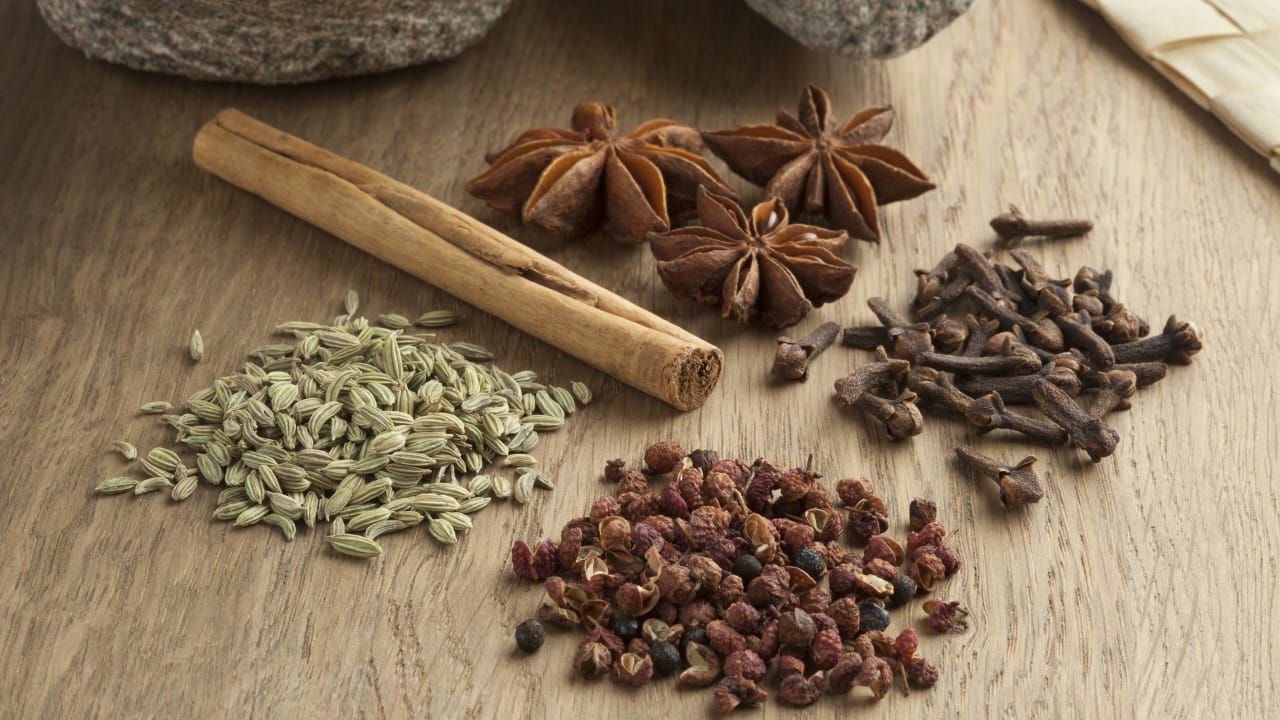 Especias variadas: rama de canela, anís estrellado, clavo, semillas de hinojo y granos de pimienta sobre madera.